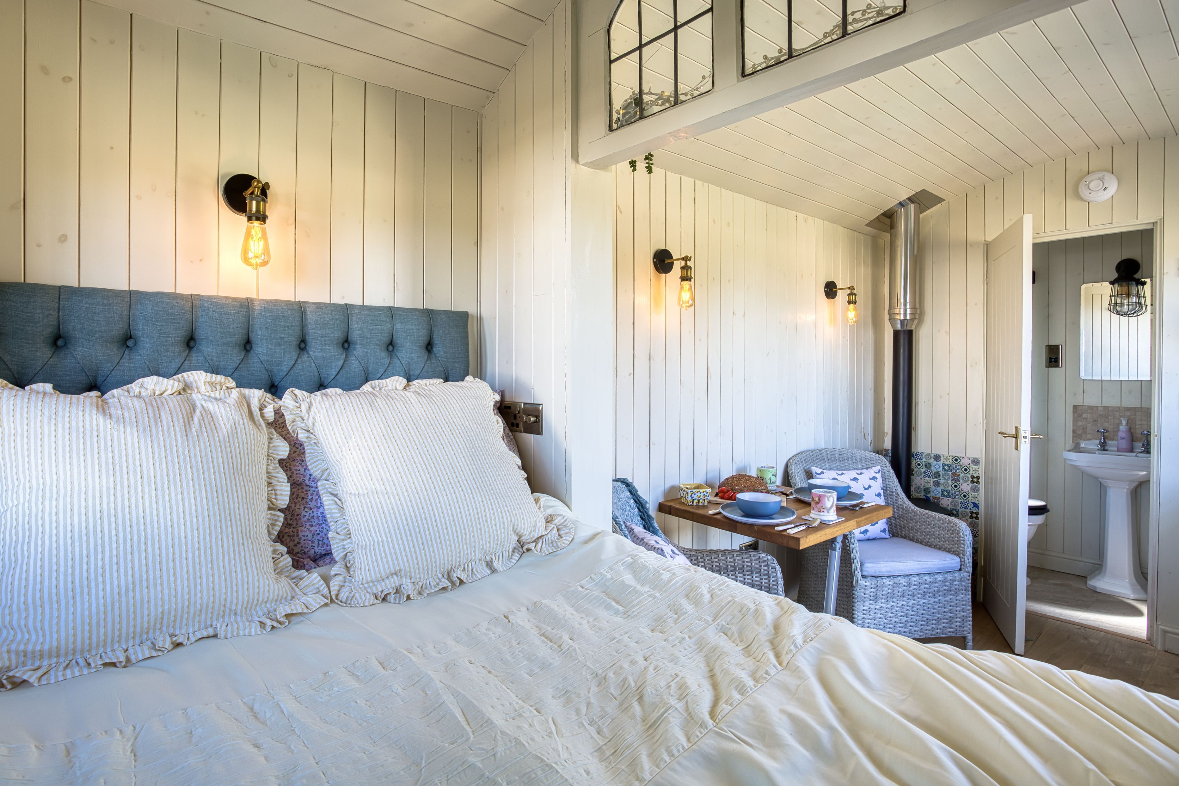 A bedroom with a large bed, a dining table with chairs, and a bathroom visible through an open door.