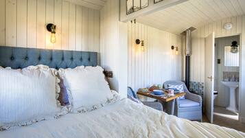 A bedroom with a large bed, a dining table with chairs, and a bathroom visible through an open door.