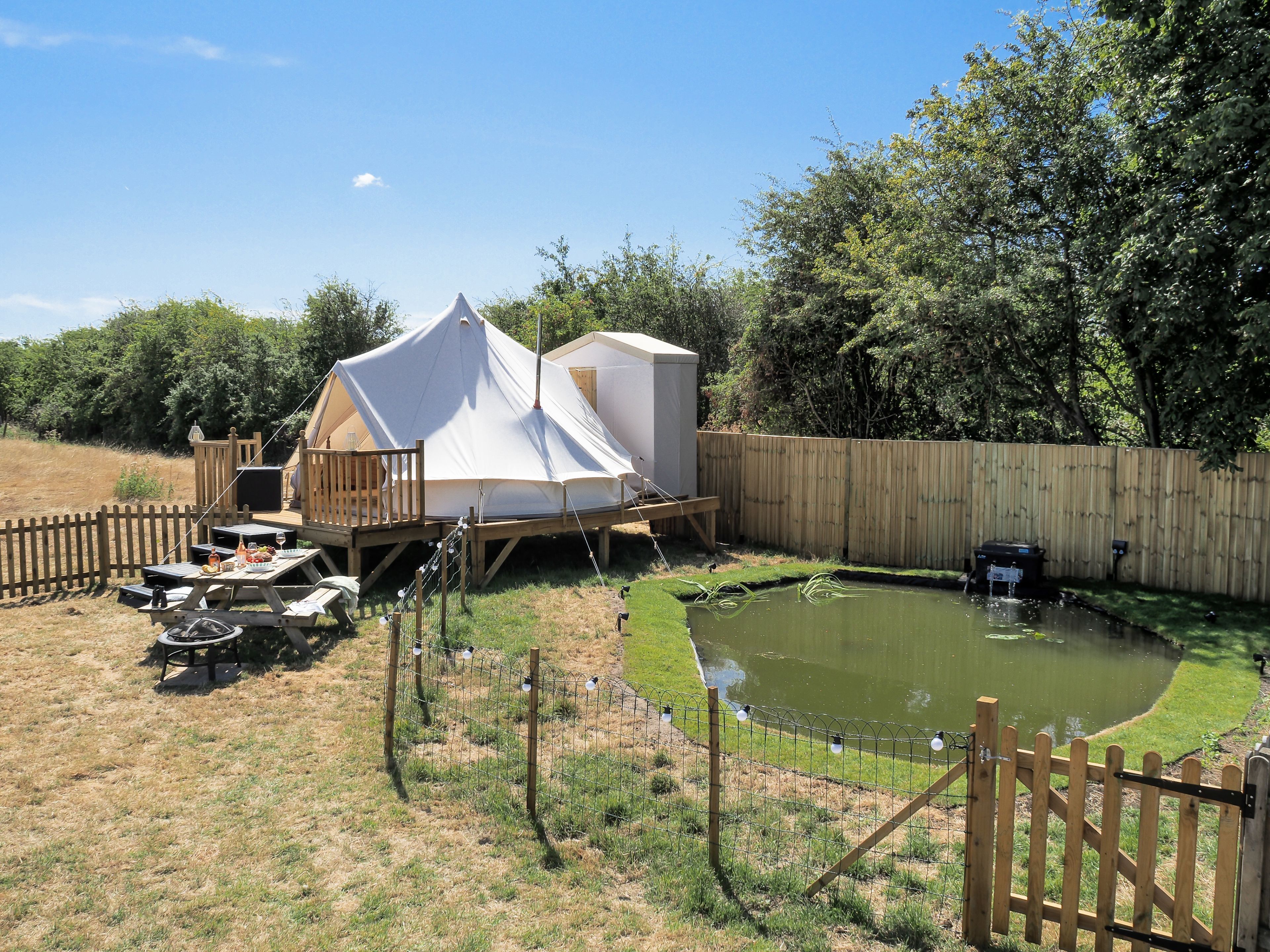 A tented accommodation with a deck and a small pond.