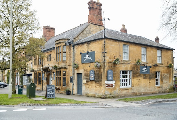 A historic building with a sign for "The Swan" pub, a traditional stone facade, and a sign indicating "Bourton Road."