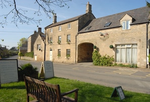 A stone building with a signboard, a bench, and a clear road in front.