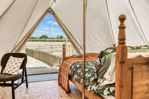 A tent with a bed, a chair, and a view of the countryside.