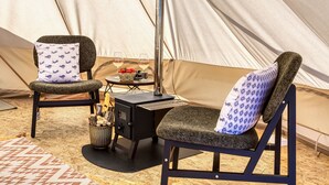 Ein Zeltinnenraum mit zwei Stühlen, einem Tisch, einem Campingkocher und einer Obstschale.