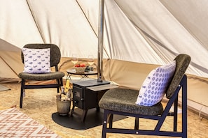 A tent interior with two chairs, a table, a portable stove, and a bowl of fruit.