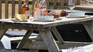 Ein Holz-Picknicktisch im Freien mit Speisen, Getränken und einer Flasche.