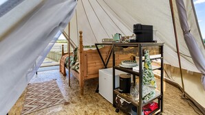 Ein Zeltinnenraum mit einem Bett, einem Tisch mit Wasserkocher und einem kleinen Kühlschrank.