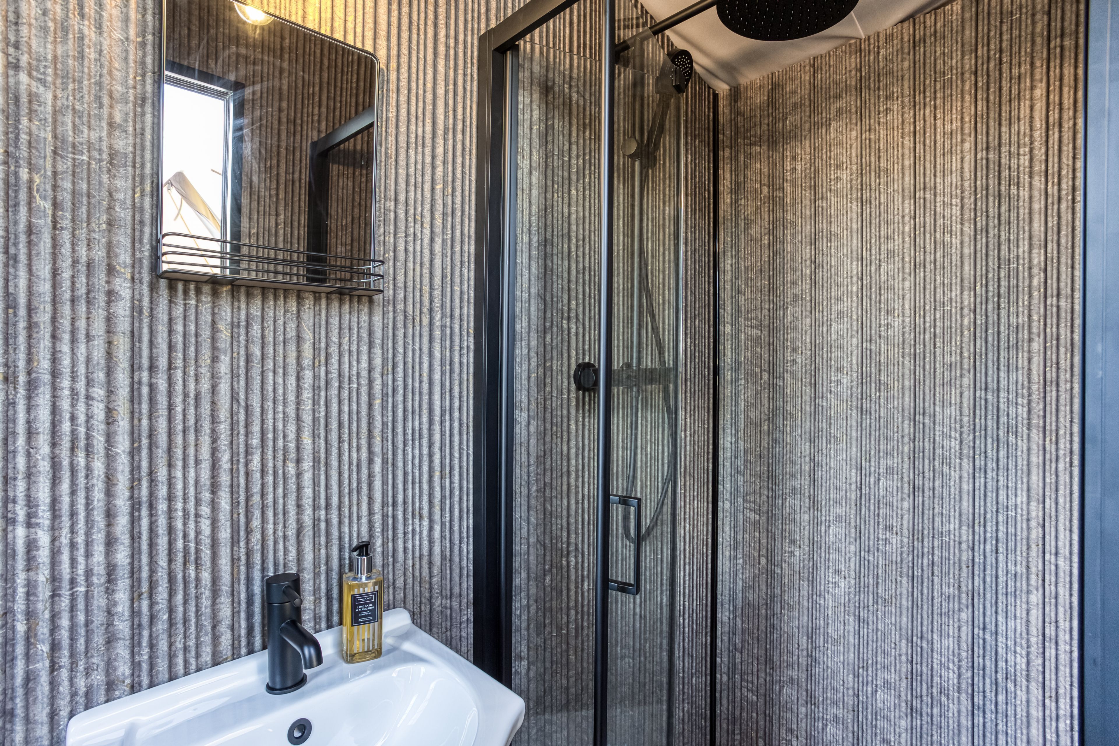 Une salle de bain avec une douche à parois de verre, un lavabo blanc et un miroir au-dessus du lavabo.