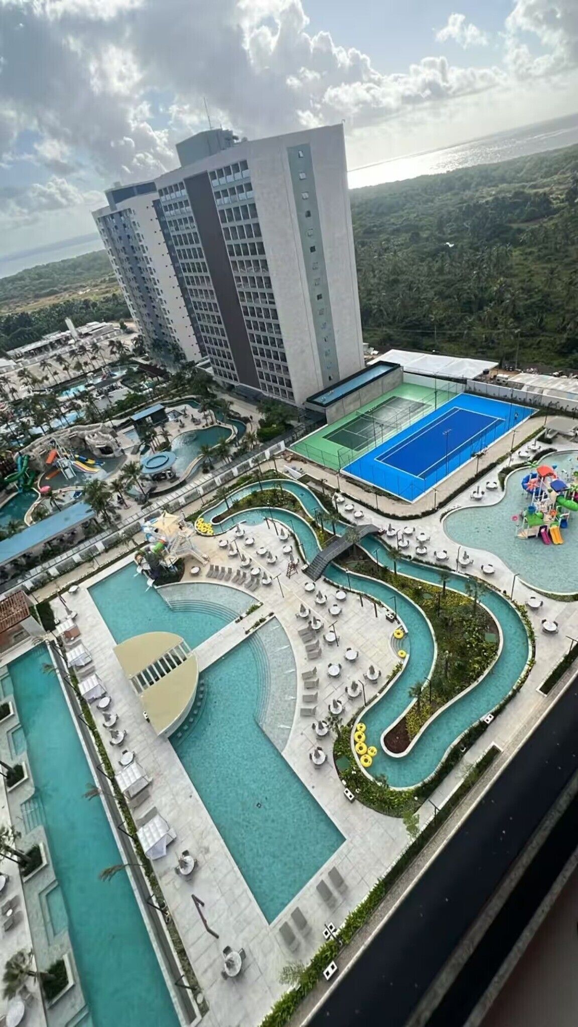 A hotel with multiple swimming pools, a large building in the background, and a view of the surrounding landscape.