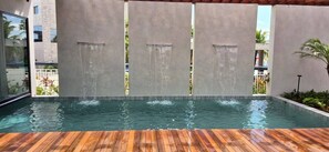 Ein Schwimmbecken mit Holzterrasse, umgeben von Mauern mit vertikalen Wasserspielen.