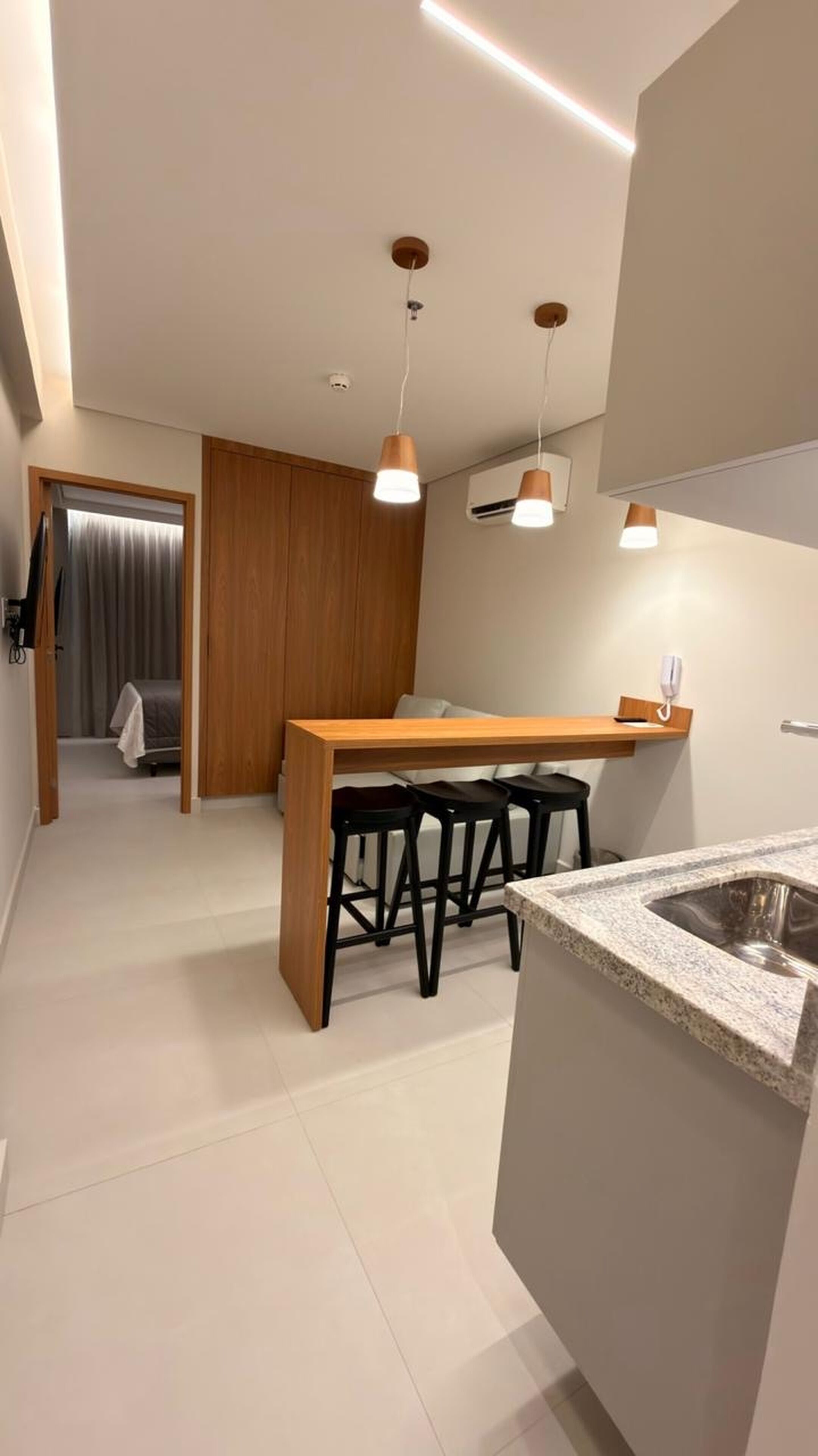 A modern kitchen with a granite countertop, wooden bar counter, and black bar stools.