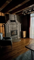 Ein Zimmer mit Kamin aus Stein, Holzbalken, einem Flachbildfernseher und einem Sessel.