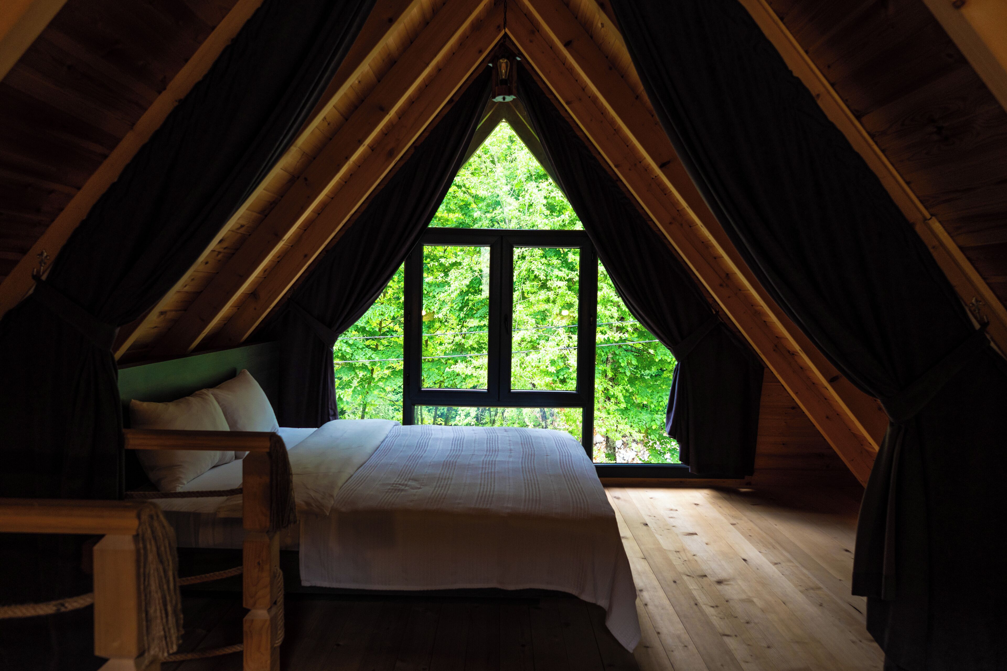 A bedroom with a bed, a chair, and a large window with a view of greenery.