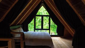 A bedroom with a bed, a chair, and a large window with a view of greenery.