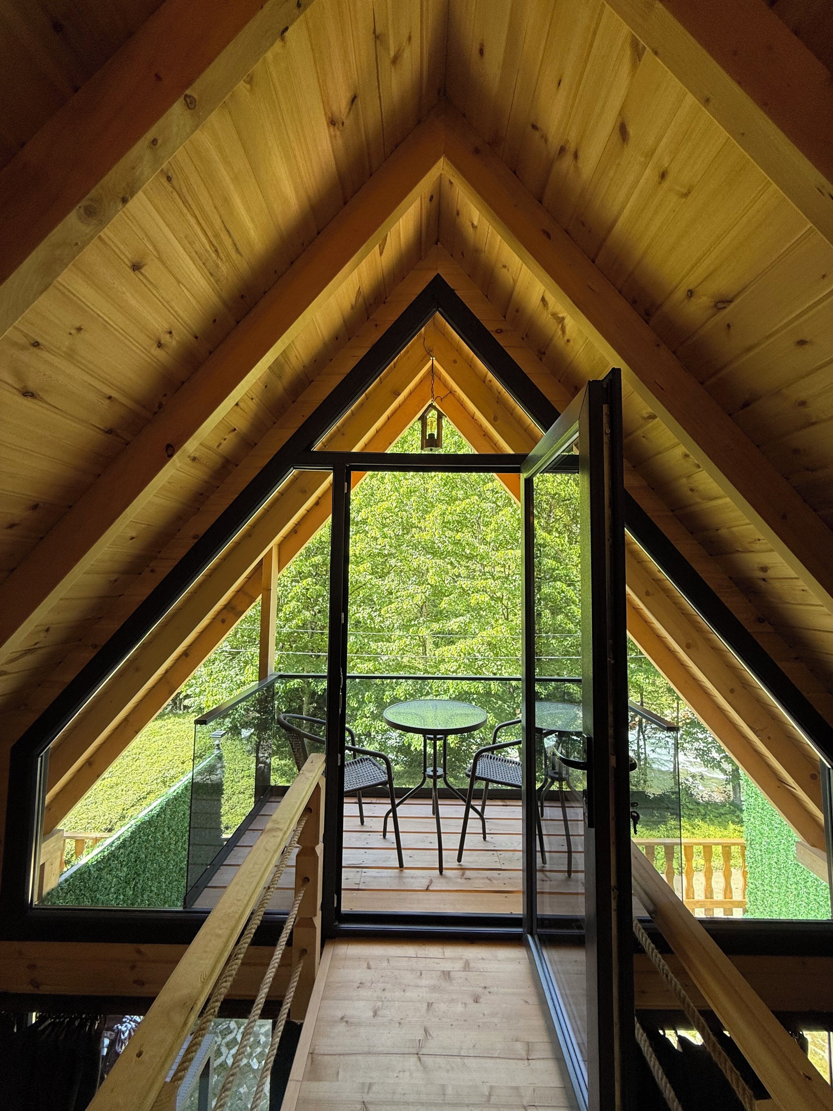 A wooden interior with a glass balcony overlooking a green landscape.