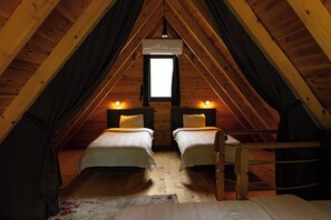 A cozy attic bedroom with two beds, a window, and a hanging light fixture.