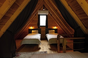 A cozy attic bedroom with two beds, a window, and a hanging light fixture.