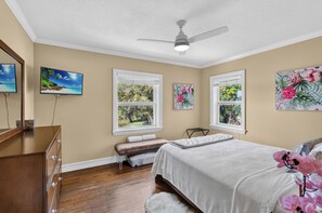 A bedroom with a bed, a bench, a ceiling fan, and two windows with views of greenery. - Lake & Lark House-4BR Lakefront Retreat Downtown (Orlando)