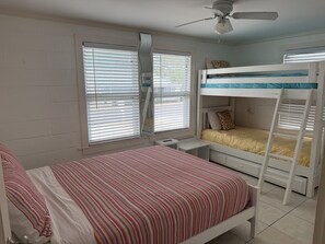 Ein Schlafzimmer mit Etagenbett, einem Einzelbett, einem Deckenventilator und einem Fenster mit Jalousien.