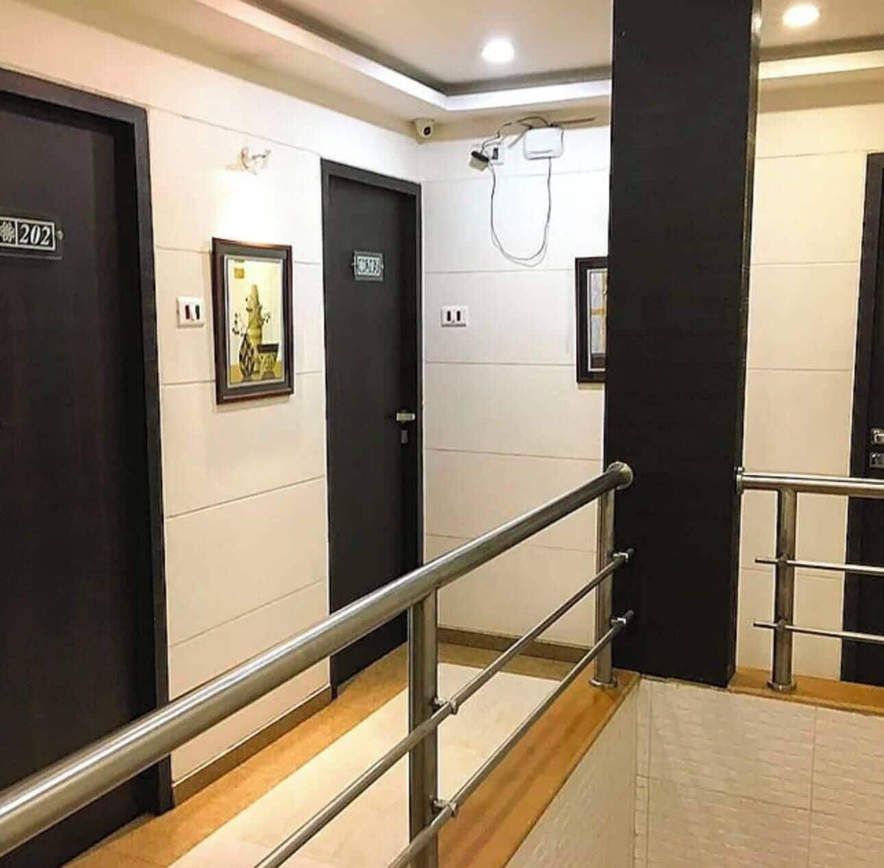 Un couloir d’hôtel avec des portes noires, une rambarde métallique et une caméra de surveillance.