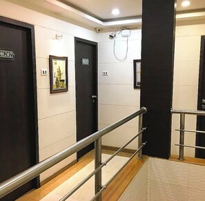 A hotel corridor with black doors, a metal handrail, and a security camera.