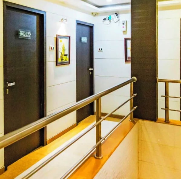 A hallway with doors, a metal handrail, and a tiled floor.