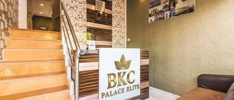 A reception desk with a sign reading 'BKC Palace Elite' and a staircase leading to an upper floor.