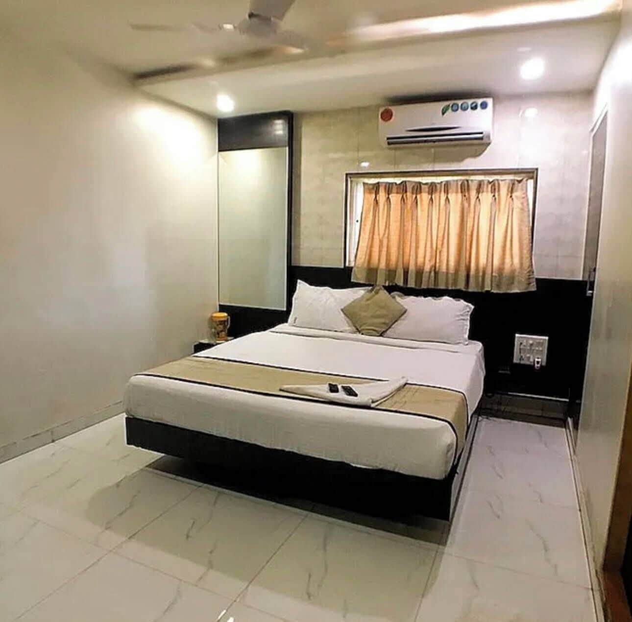 Une chambre d’hôtel avec un lit, une table de chevet, un appareil de climatisation et une fenêtre avec des rideaux.