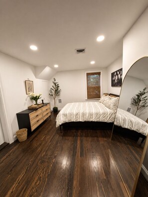 Une chambre à coucher avec un lit, une commode, un miroir et une fenêtre avec des stores.