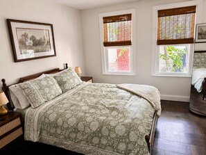 A bedroom with a bed, nightstands, a framed picture, and windows with blinds.