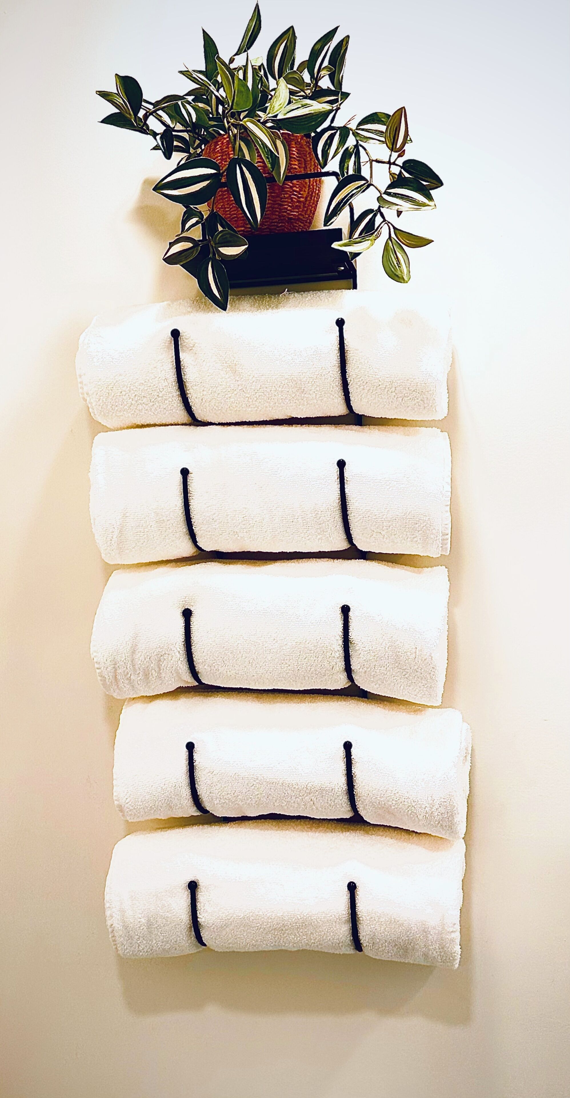 Ein an der Wand befestigter Handtuchhalter mit sechs weißen Handtüchern und einer Topfpflanze.