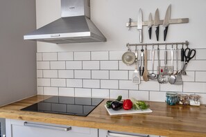 Una cocina con tope de inducción negro, campana de acero inoxidable y varios utensilios colgados en un colgador.