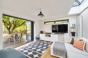 Una sala de estar moderna con un televisor grande, un sofá y una zona de comedor con una mesa y sillas.