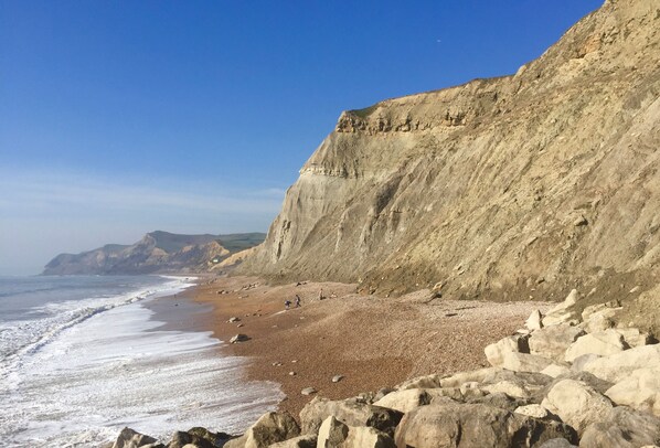 Paisagem costeira com uma praia rochosa, falésias e céu claro.