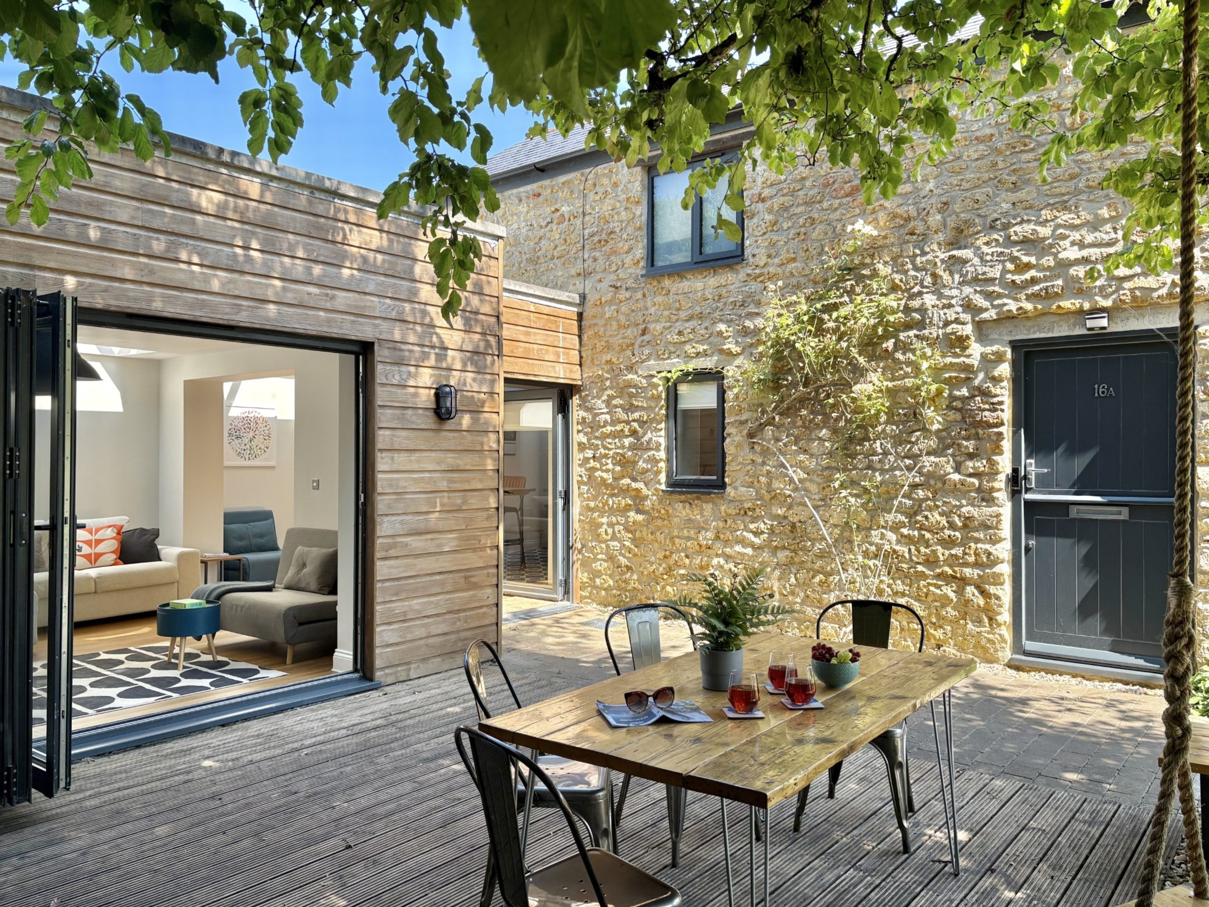 Une terrasse en bois avec une table dressée pour le repas, une plante en pot et une vue sur un bâtiment en pierre.