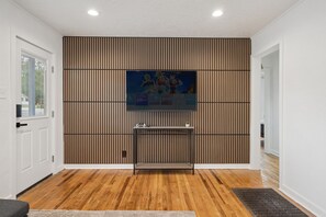 A hallway with a wooden floor, a wall-mounted TV, and a door on the left. - Downtown 2 bedroom ranch home with hot tub, AC and all the amenities! (Colorado Springs)