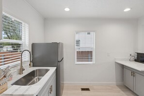 A modern kitchen with a stainless steel sink, a refrigerator, and a window with blinds. - Downtown 2 bedroom ranch home with hot tub, AC and all the amenities! (Colorado Springs)