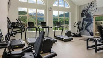 A gym with various cardio machines, large windows, and a mountain view.