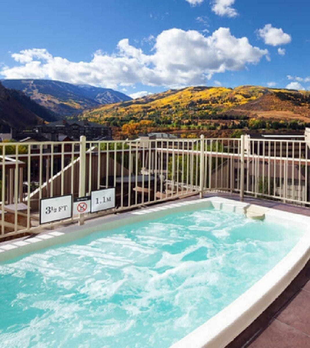 Una piscina con vistas a montañas y un área cercada con señales que indican la profundidad.