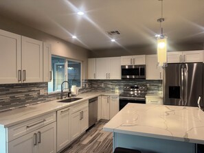 A modern kitchen with white cabinets, stainless steel appliances, a marble countertop, and a pendant light. - Wonderful 4-bedroom Home Base in Phoenix- Freeway Access- Close to everything! (Phoenix)