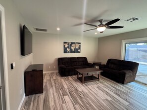 A living room with a ceiling fan, a flat-screen TV, a dark brown sofa, a wooden coffee table, and a world map artwork on the wall. - Wonderful 4-bedroom Home Base in Phoenix- Freeway Access- Close to everything! (Phoenix)