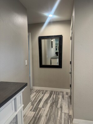 A hallway with a wooden floor, a mirror with a black frame, and a door on the right. - Wonderful 4-bedroom Home Base in Phoenix- Freeway Access- Close to everything! (Phoenix)