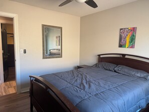 Ein Schlafzimmer mit einem Bett, einem Deckenventilator, einem Spiegel und einem Bild an der Wand.