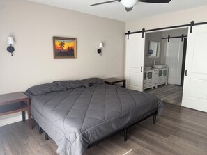 A bedroom with a bed, bedside tables, a ceiling fan, a painting, and a bathroom with a sink and cabinets. - Wonderful 4-bedroom Home Base in Phoenix- Freeway Access- Close to everything! (Phoenix)