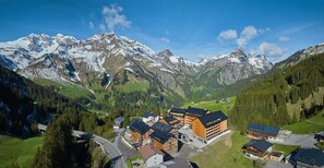 Ein Gebirgsort mit Chalet-ähnlichen Gebäuden, einer Seilbahn und schneebedeckten Gipfeln im Hintergrund.