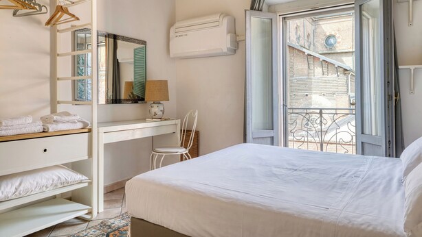 A bedroom with a bed, a desk, a chair, a wardrobe, and a window with a view of a building. - Bright 1BR with Balcony in Navigli (Milano)