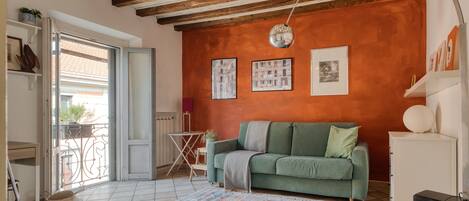 Una sala de estar con un sofá verde, un tapete estampado y piso de baldosas.