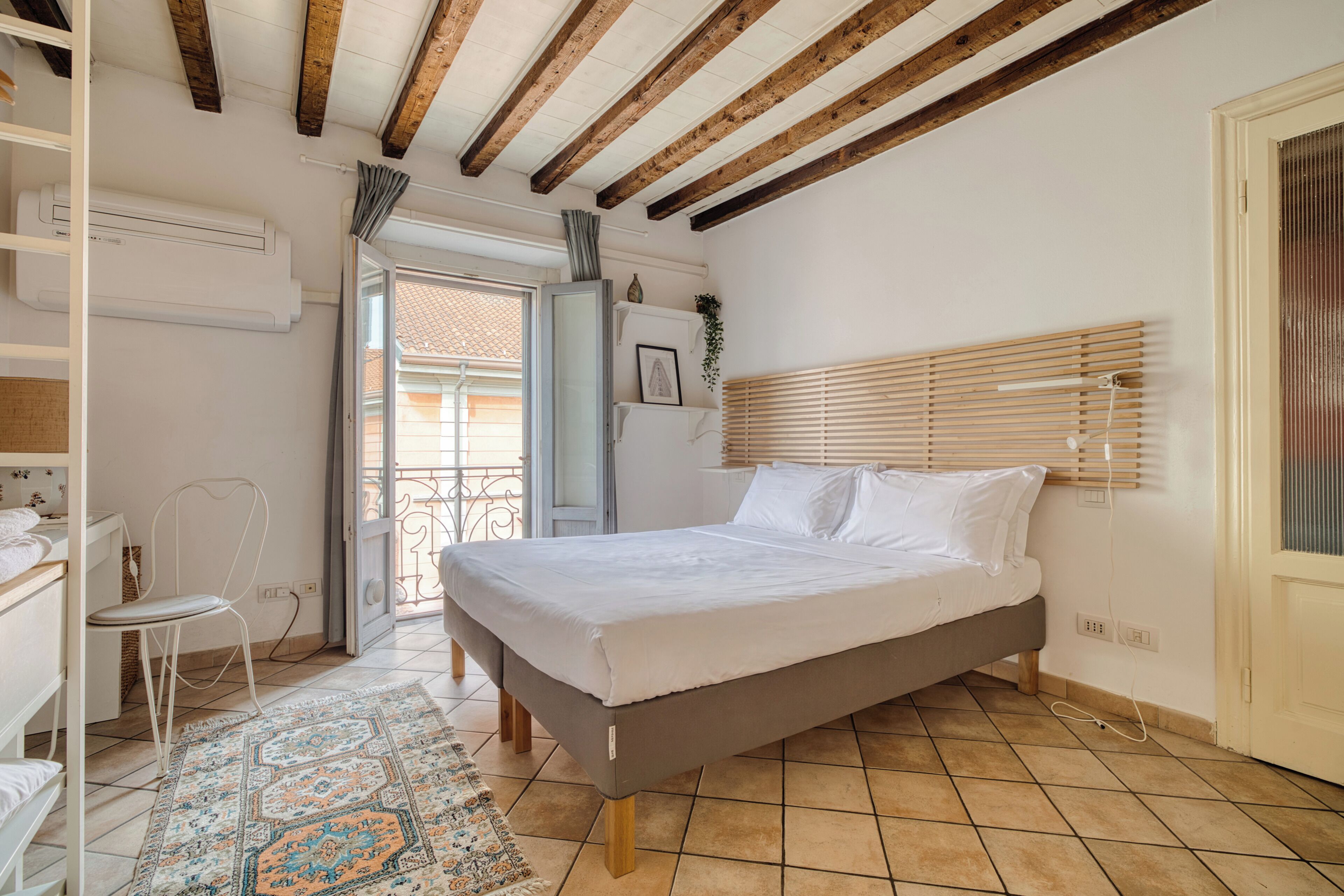 A bedroom with a bed, a chair, a desk, and a window with blinds.