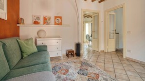 A living room with a green sofa, a white dresser, and a patterned rug. There is a hallway leading to another room. - Bright 1BR with Balcony in Navigli (Milano)