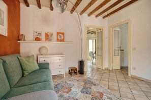 A living room with a green sofa, a white dresser, and a patterned rug. There is a hallway leading to another room. - Bright 1BR with Balcony in Navigli (Milano)