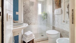 A bathroom with a glass shower enclosure, a white toilet, and a sink with a blue-tiled backsplash. - Bright 1BR with Balcony in Navigli (Milano)